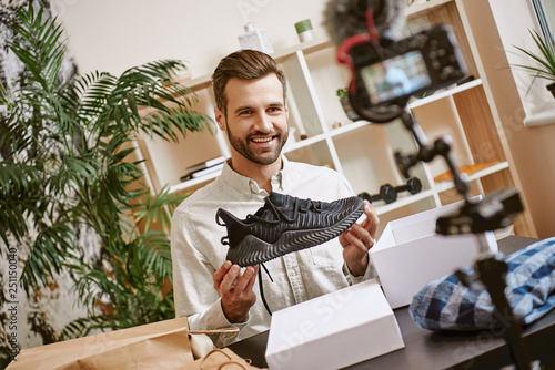 Sport shoes. Cheerful male blogger holding black sneakers while recording new video for his blog. photo