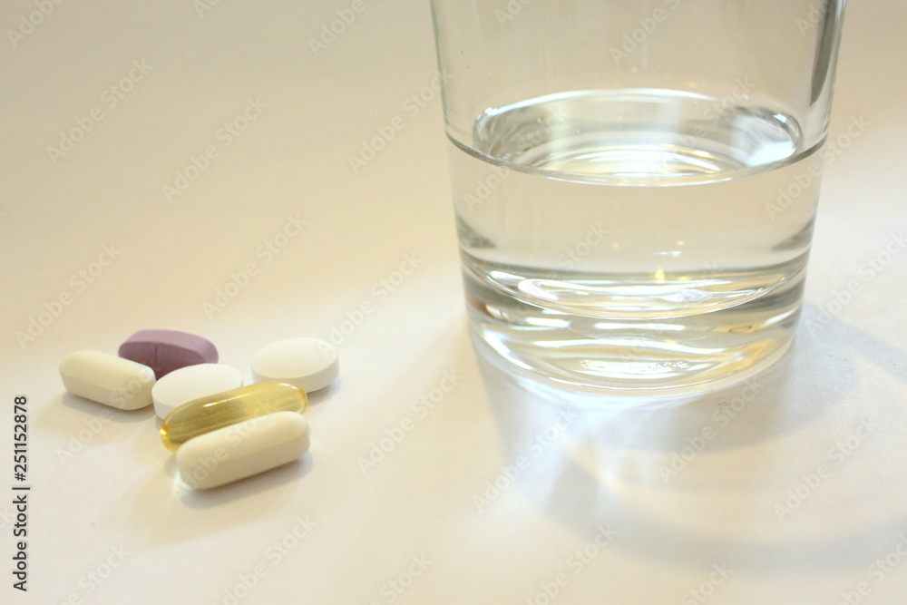 A glass of water with a selection of pills at the side. Copy space. Taking medication concept A glass of water with a selection of pills at the side. Copy space. Taking medication concept