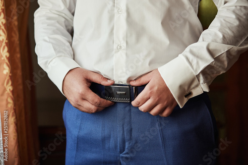 Businessman putting on a belt, fashion and clothing concept,groom getting ready in the morning before ceremony