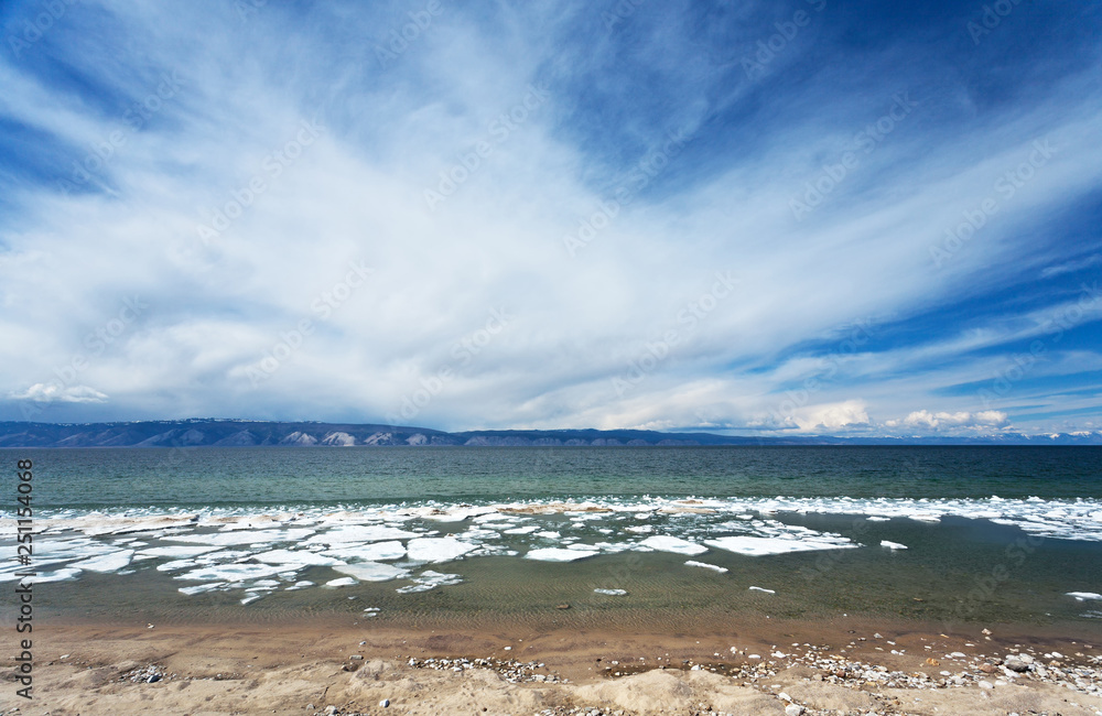 Beautiful clouds over the sandy beach during the ice drift. The change of seasons. Spring landscape of the Small Sea Strait of the Siberian Lake Baikal