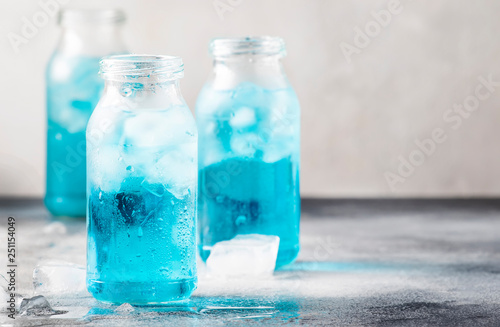 Sport and fitness drink concept, very cold refreshing isotonic blue water in bottles, gray table background, selective focus