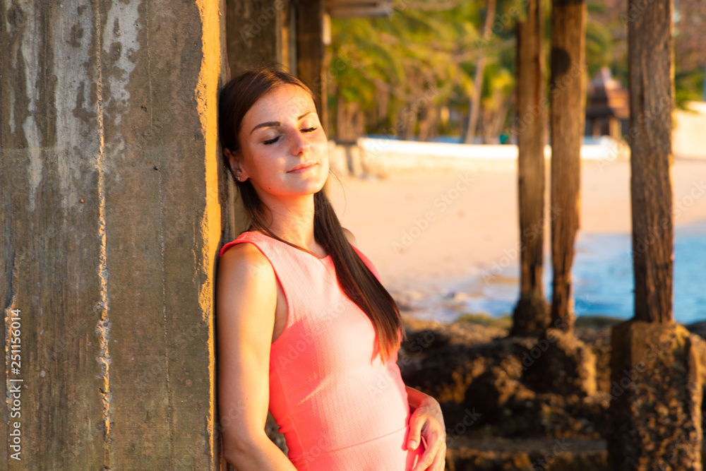 Fototapeta premium A woman stands on the beach in the evening. The girl at sunset. Attractive young lady enjoying the last rays of the sun. copy space place for text