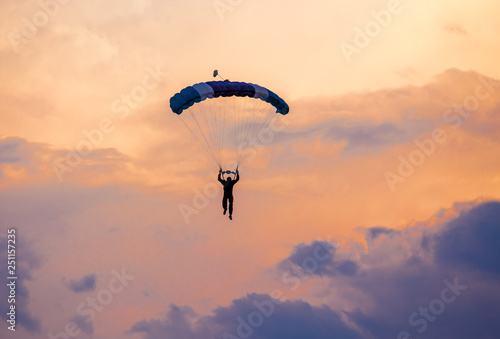 Parachutist falling from the sky in evening sunset dramatic sky. Recreational sport, Paratrooper silhouette on colored sky.