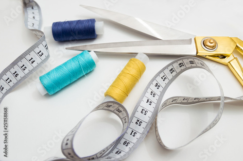 golden scissors, blue, blue and yellow threads, measuring tape lying on a white background, a set for cutting and sewing