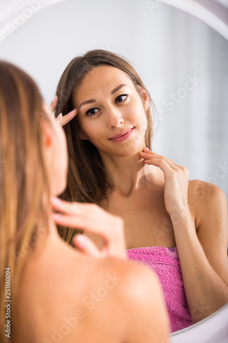 woman examining her face by looking at it in mirror