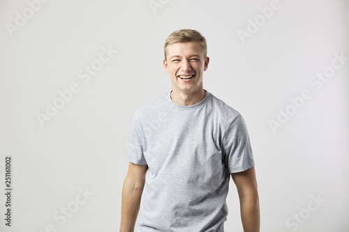 Smiling blond guy dressed in a white t-shirt stands on the white background in the studio
