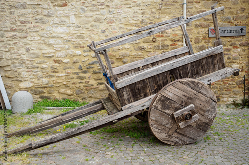 Old wooden cart with a stone masonry wall on the background with a cartiera sign (paper mill in Italian language).