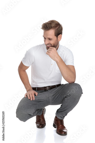 lughing crouched smart casual man thinks and looks to side