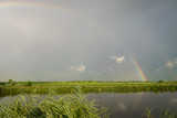 A bright colorful double rainbow over the dutch countryside near Gouda, Holland. The rainbow is reflected in the water of the canal.