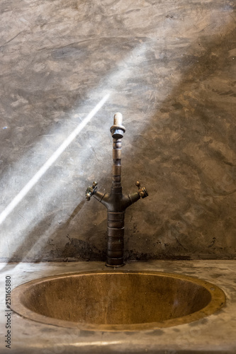 Luxury faucet with golden sink on the raw concrete counter in vintage bathroom. Line of sunlight hit the classic water tap