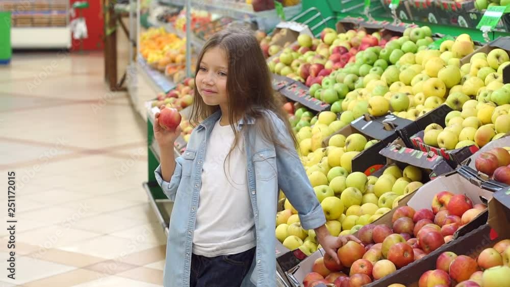 Portrait of a little girl in a supermarket with an Apple in her hands on the background of shelves with fruit. Slow motion. Portrait of a little girl in a supermarket with an Apple in her hands on the background of shelves with fruit. Slow motion.