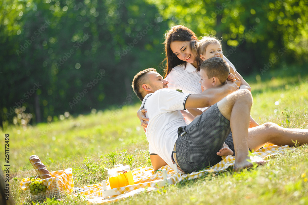 Fototapeta premium Young family having picnic outdoor. Mother, father and their kids having fun in the park. Summer resting at the nature.