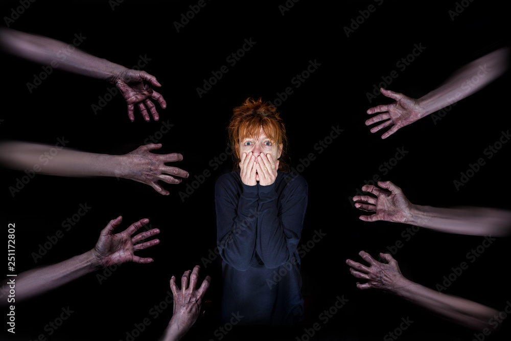 Several hands reach for a frightened, panicked woman against a black background