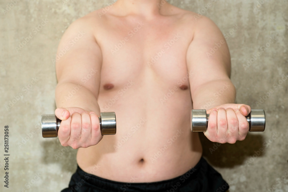 The torso of a young man performs a close-up exercise with dumbbells against a concrete wall.