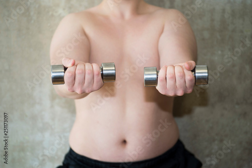 The torso of a young man performs a close-up exercise with dumbbells against a concrete wall.