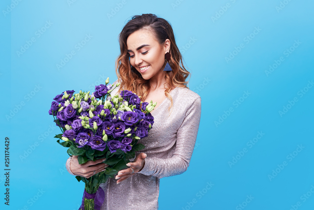 Young happy smiling redhead woman holding bouquet of violet spring flowers isolated on blue background. Festive bouquet in honor of women's day on March 8 or birthday Young happy smiling redhead woman holding bouquet of violet spring flowers isolated on blue background. Festive bouquet in honor of women's day on March 8 or birthday