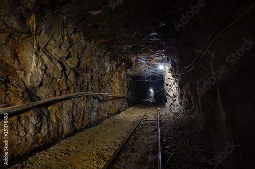Underground gold ore mine shaft tunnel gallery passage with rails and light