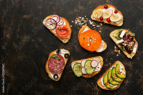 A variety of toast with vegetables, fruits, salmon and sausage on a dark background, top view. Sandwiches with a variety of fillings.