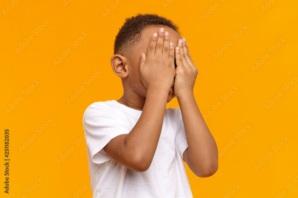 Human emotions, reaction and body language. Unrecognizable black child playing hide and seek. Dark skinned African boy covering face with both hands, feeling scared, ashamed or hiding tears Human emotions, reaction and body language. Unrecognizable black child playing hide and seek. Dark skinned African boy covering face with both hands, feeling scared, ashamed or hiding tears