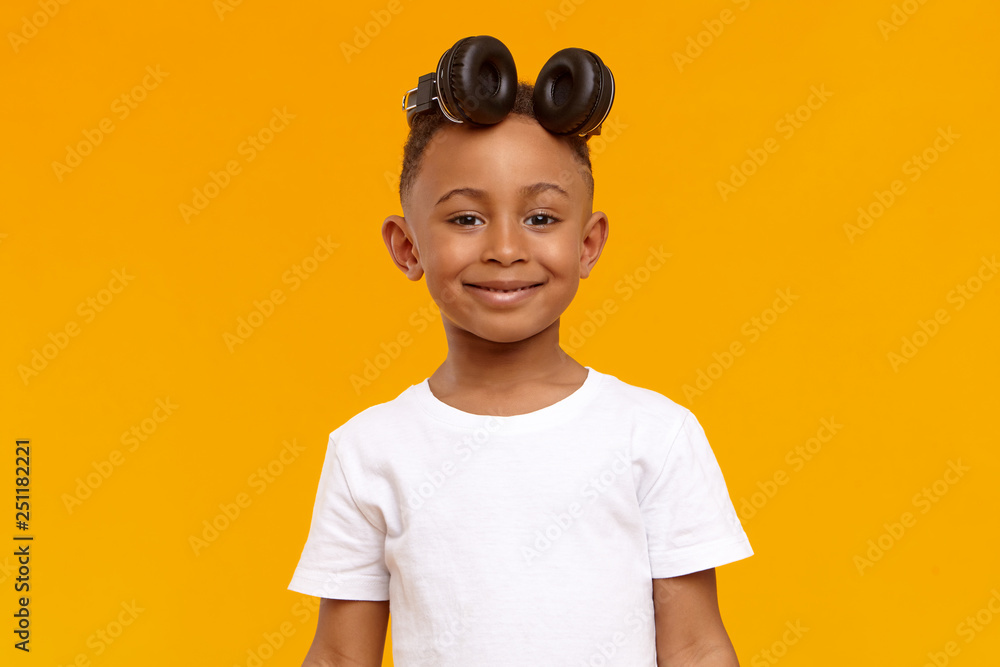 Modern technology, gadgets, children and generation concept. Portrait of cute friendly African American little boy looking at camera with cheerful smile, wearing wireless headset on top of his head Modern technology, gadgets, children and generation concept. Portrait of cute friendly African American little boy looking at camera with cheerful smile, wearing wireless headset on top of his head