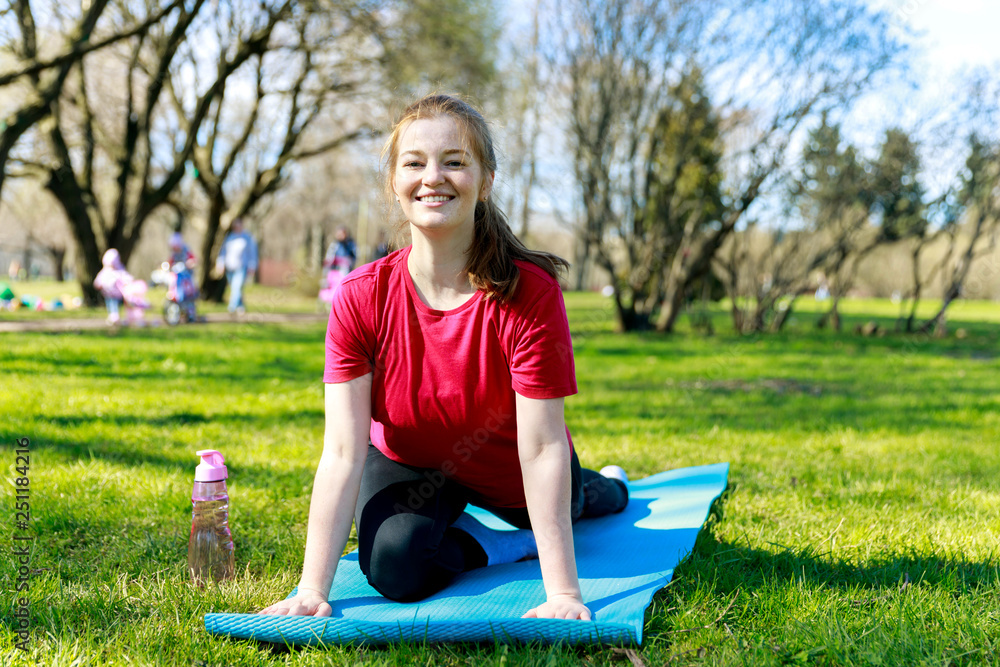 Fototapeta premium Smiling girl in the park exercise on the yoga mat, Pigeon Pose