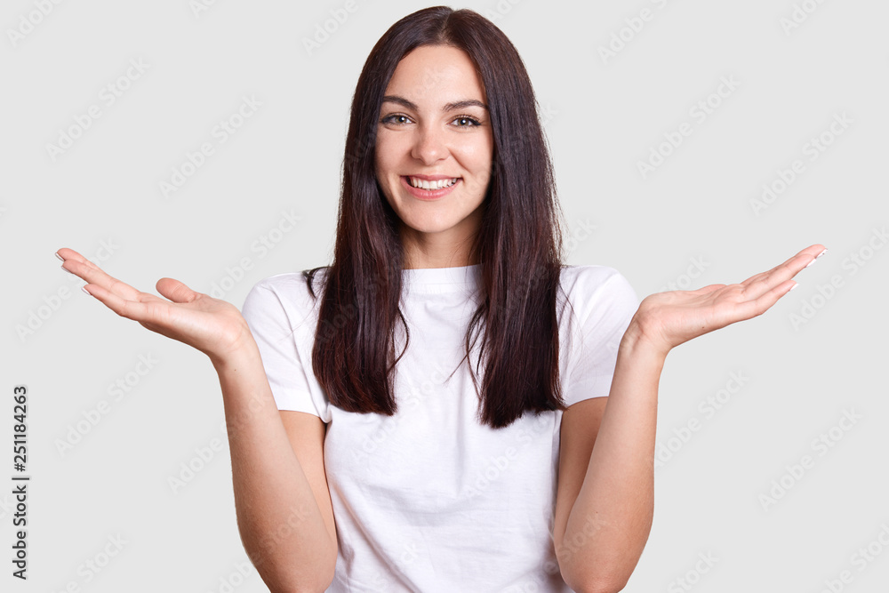 Isolated shot of joyful brunette pretty woman laughing happily when she sees or hears something funny, has medium dark hair, poses on gray studio wall. Concept of happiness and positive emotions. Isolated shot of joyful brunette pretty woman laughing happily when she sees or hears something funny, has medium dark hair, poses on gray studio wall. Concept of happiness and positive emotions.