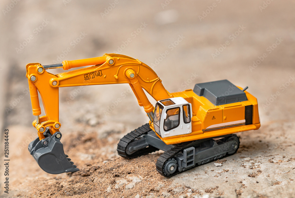 Yellow excavator model toy performs excavation work on a construction site. (Image stacking technique) Yellow excavator model toy performs excavation work on a construction site. (Image stacking technique)