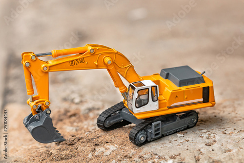 Yellow excavator model toy performs excavation work on a construction site. (Image stacking technique)