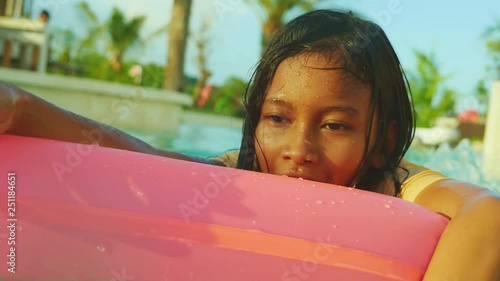 handheld shot of young happy and cute female child having fun with inflatable airbed in holidays resort swimming pool smiling carefree and cheerful in young girl vacations concept