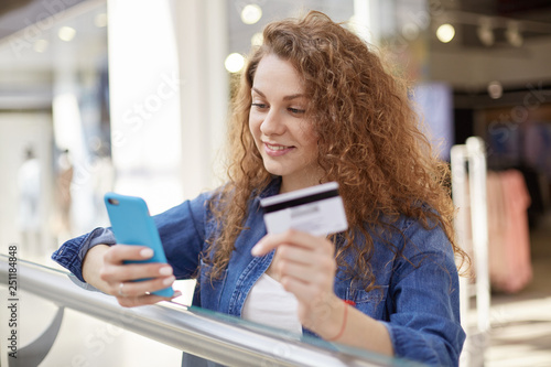 Stylish and bright woman reads notice that lot of money was received on account. Agitated mistress checks information on internet. She holds credit card in hand, checks availability of funds. photo