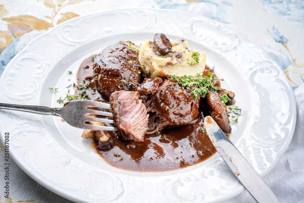 Traditional German braised pork cheeks in brown red wine sauce with mushroom and mashed potatoes as closeup on a classic design white plate Traditional German braised pork cheeks in brown red wine sauce with mushroom and mashed potatoes as closeup on a classic design white plate