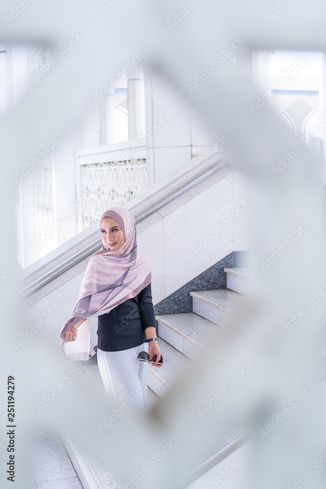 Close up portrait of happy young Asian woman wearing hijab, Islamic stylish modern fashion, smiling and posing on stairs with pattern frame at Shah Alam Mosque. Close up portrait of happy young Asian woman wearing hijab, Islamic stylish modern fashion, smiling and posing on stairs with pattern frame at Shah Alam Mosque.