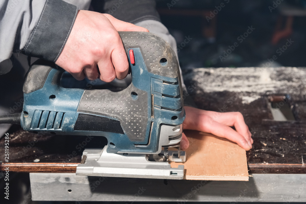 Close up of carpenter's hands working power tools for processing wood. Power Jigsaw Close up of carpenter's hands working power tools for processing wood. Power Jigsaw