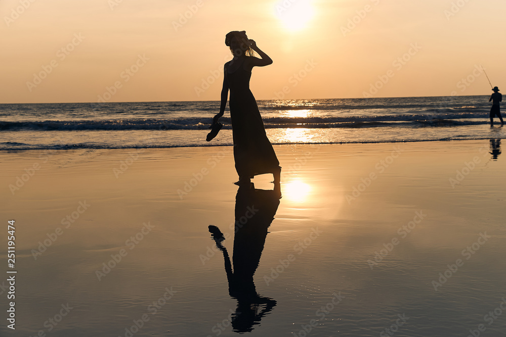 contrast silhouette of a young slender woman against the background of a Sunny sunset, the sea and the sandy beach. warm evening tones and reflections of the figure on the wet sand