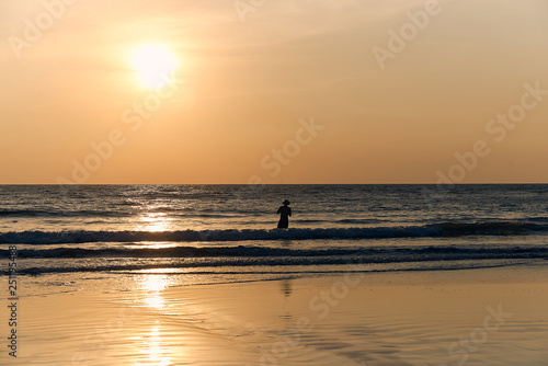 silhouette of a fisherman man against the sunset and the sea. sand beach and wave, tinted with warm colors