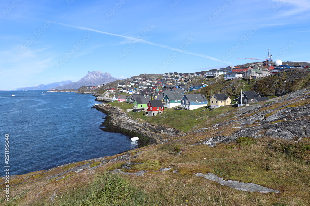 Nuuk, capital of Greenland. Town in Greenland with colorful houses on the shore of the blue bay where an iceberg floats