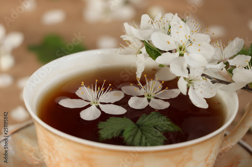 Spring  delicious  delicate tea with cherry flowers and raspberry leaves in a light brown cup close-up