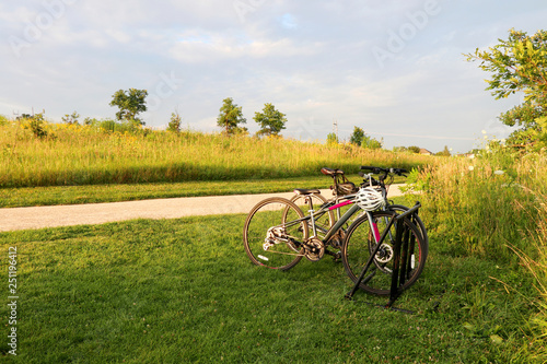 Beautiful rural summertime evening nature background. Scenic view with wild grasses field, rural road and pair of parked bicycles in a foreground during sunset. Healthy lifestyle concept. photo