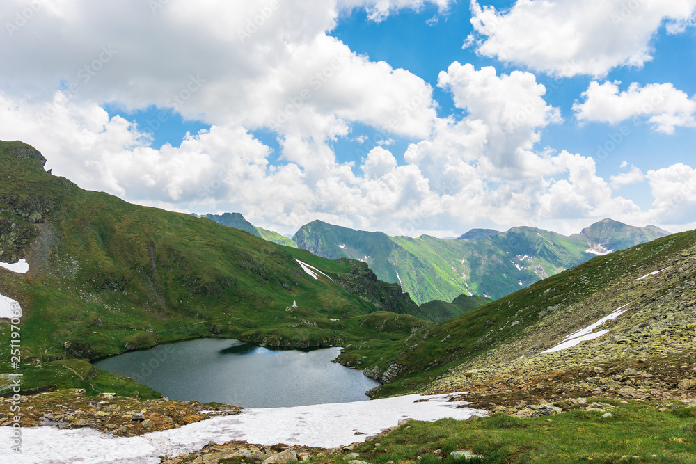 summer time in romanian carpathians. beautiful landscape of fagaras mountains. lake capra down in the valley. fluffy clouds above the ridge. view from the slope of Saua Caprei