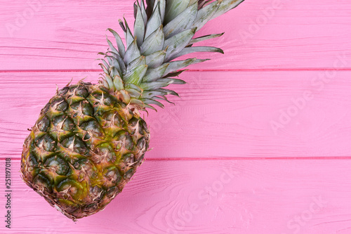 Fresh single ananas on color wooden background. Flat lay fresh ripe tropical pineapple with its crown of leaves on pink wooden surface with text space.