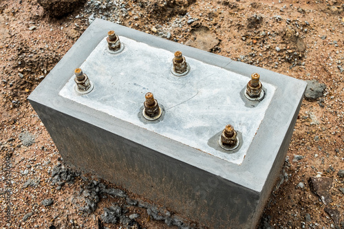 Concrete footing supporting steel beam building under construction. Welded base plate and connecting,steel plate on concrete floor.