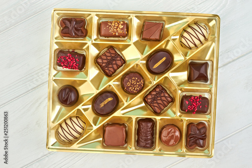 Chocolate candies in box, top view. Assorted candies in golden box on white wooden background.