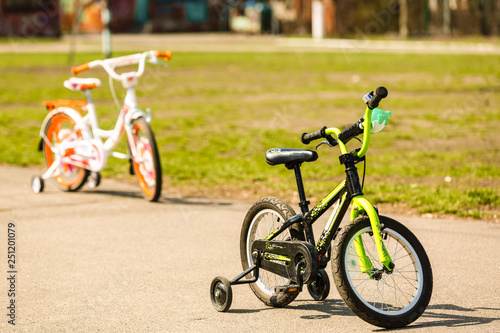 A children's low two-wheeled white-purple bicycle with extra side wheels stands in the middle of the park and lives its little owner.