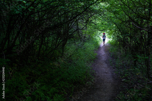 Schilderij op canvas the girl in the shorts and the hat goes along the path from the dark thicket