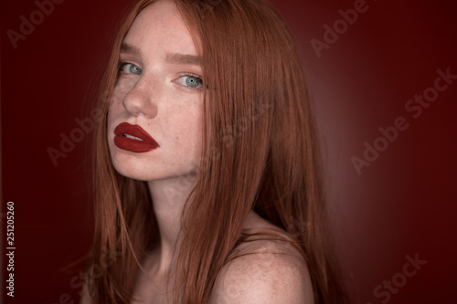 The portrait of a young redhead lady isolated over a red background