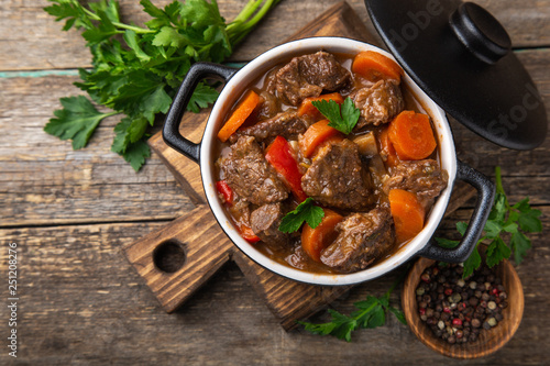 beef stew with vegetables in black pot on dark wooden background,