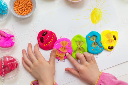 Little girl playing with plasticine. Play clay caterpillar decorated with cereals. Creative learning activities