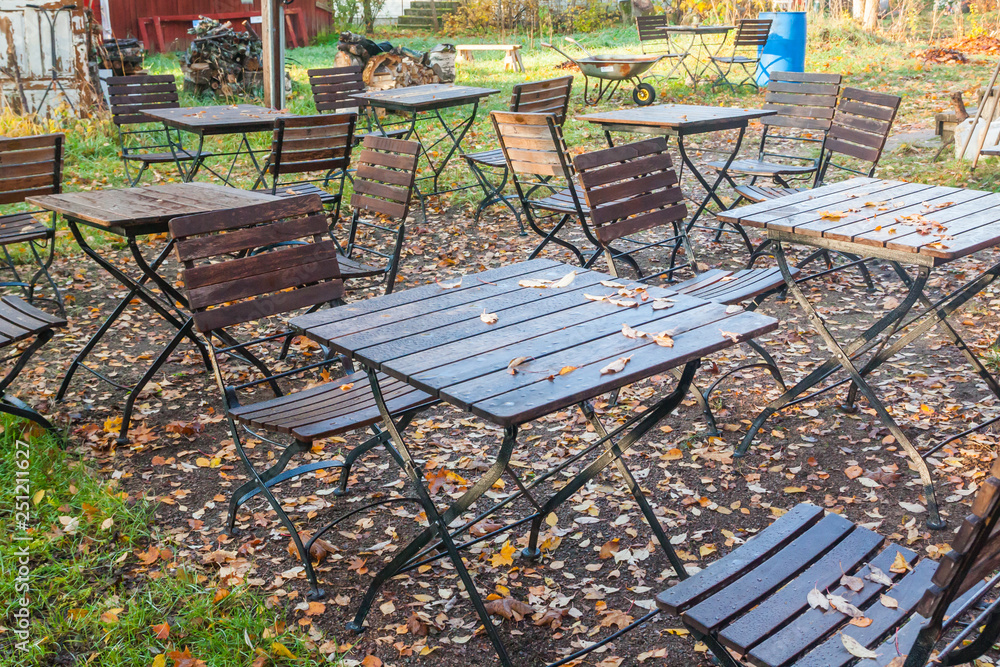 Beautiful autumn in old outdoor cafe in the park - wet tables and chairs with colorful foliage.