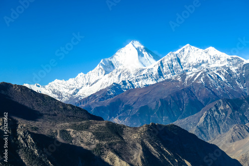 Harsh slopes of Manang Valley, Annapurna Circus Trek, Himalayas, Nepal, with the view on Annapurna Chain and Gangapurna. Dry and desolated landscape.  High mountain peaks, covered with snow. photo