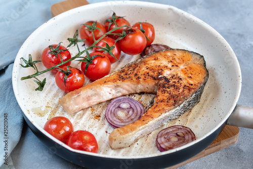Fried salmon in a frying pan with tomatoes and red onion.